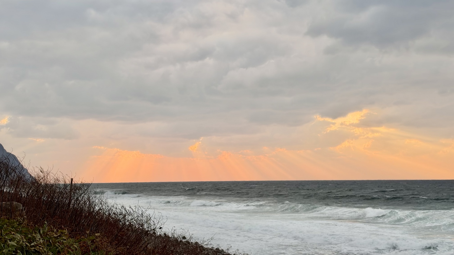 岩内町敷島内から見た海岸と山。波が立つ海の上に厚い雲が広がっている。