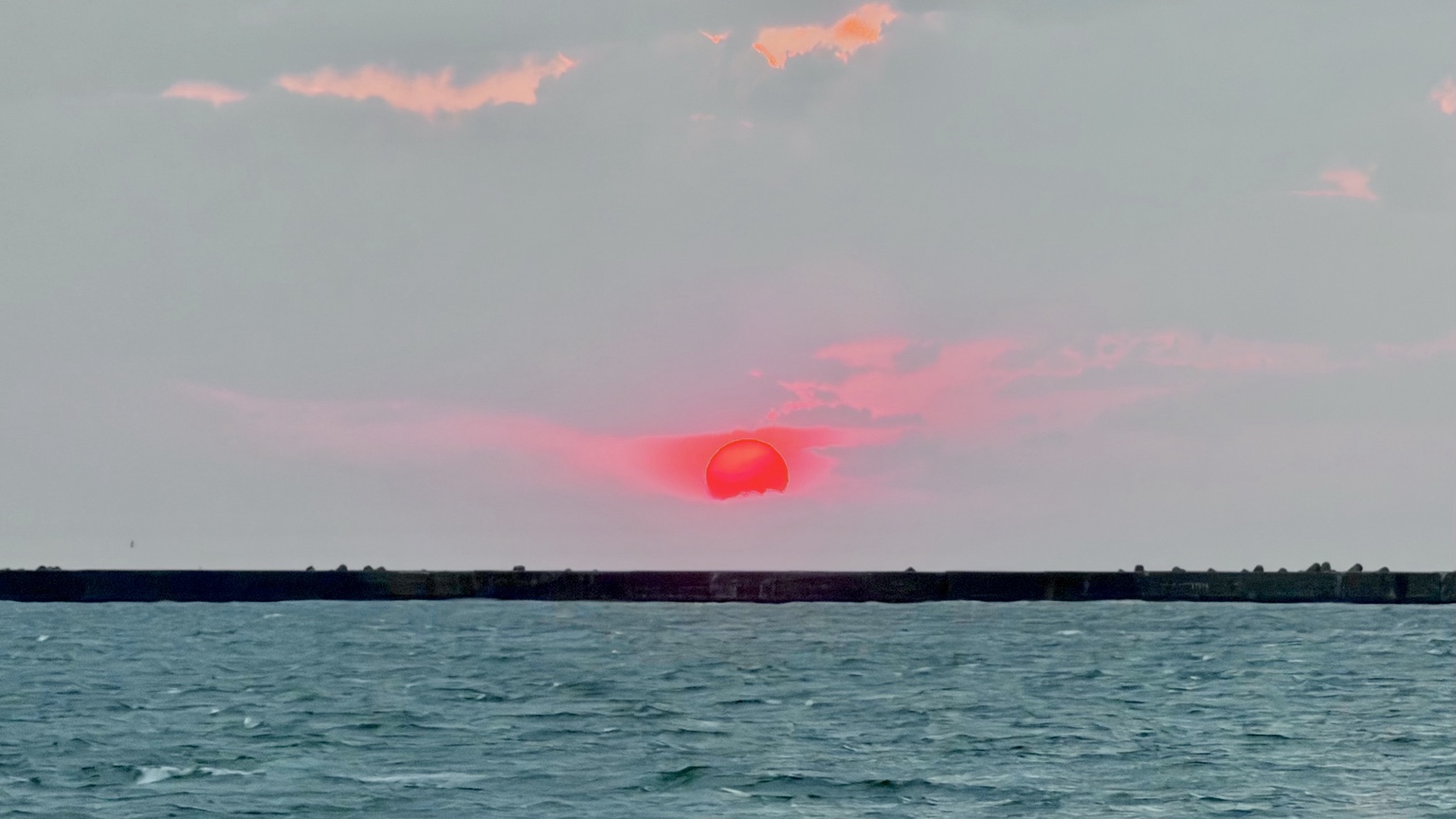 岩内町の新港東埠頭から見た夕日。雲の間から日没前の光が差している。