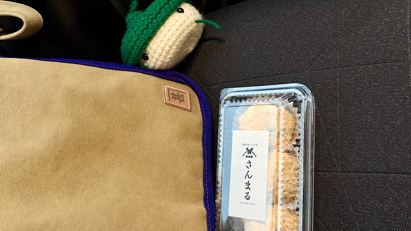 布製バッグと編みぐるみのそばに置かれた「さんまる」の包装食品